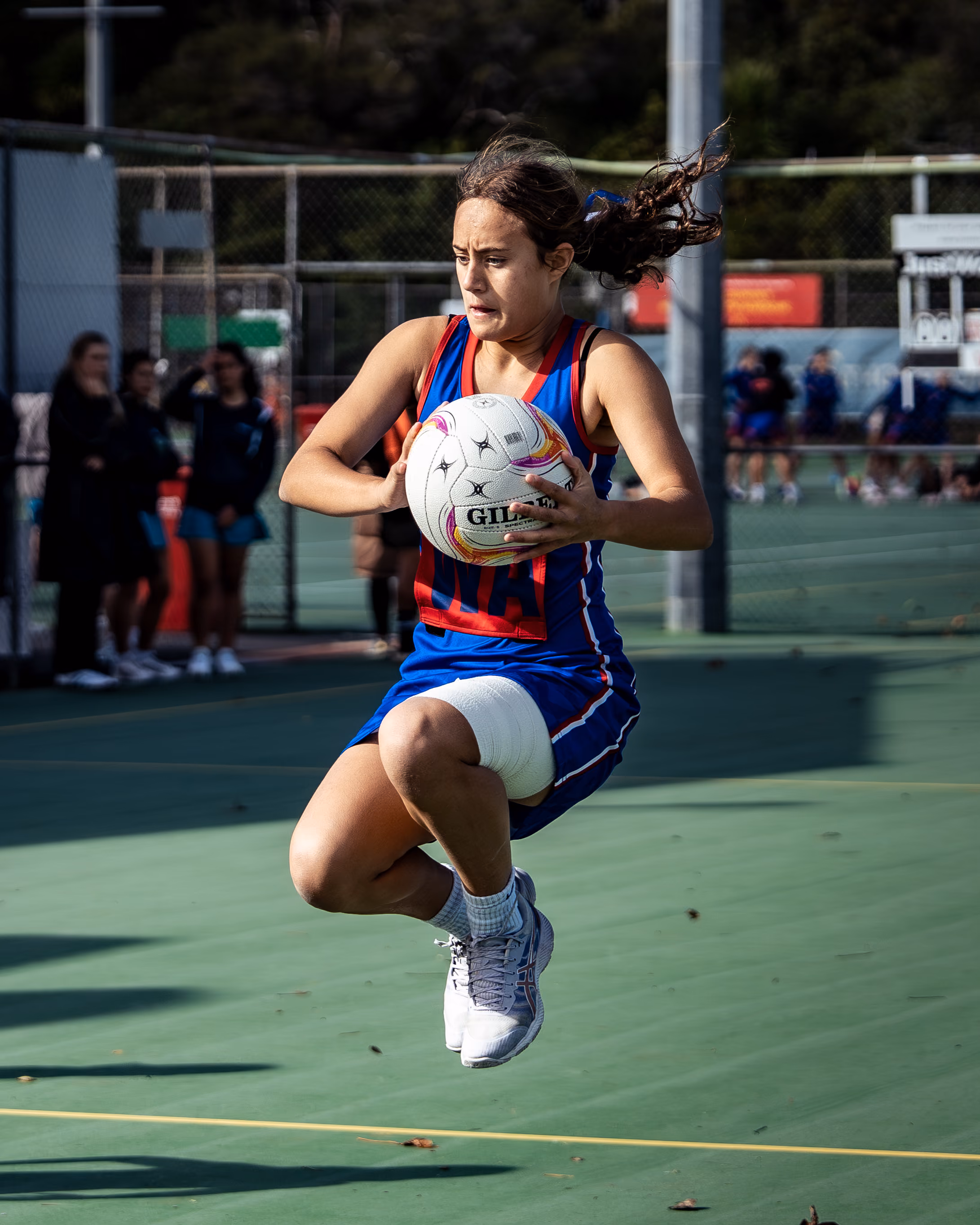 A focused Rosehill College netball player leaping to catch the ball during a game